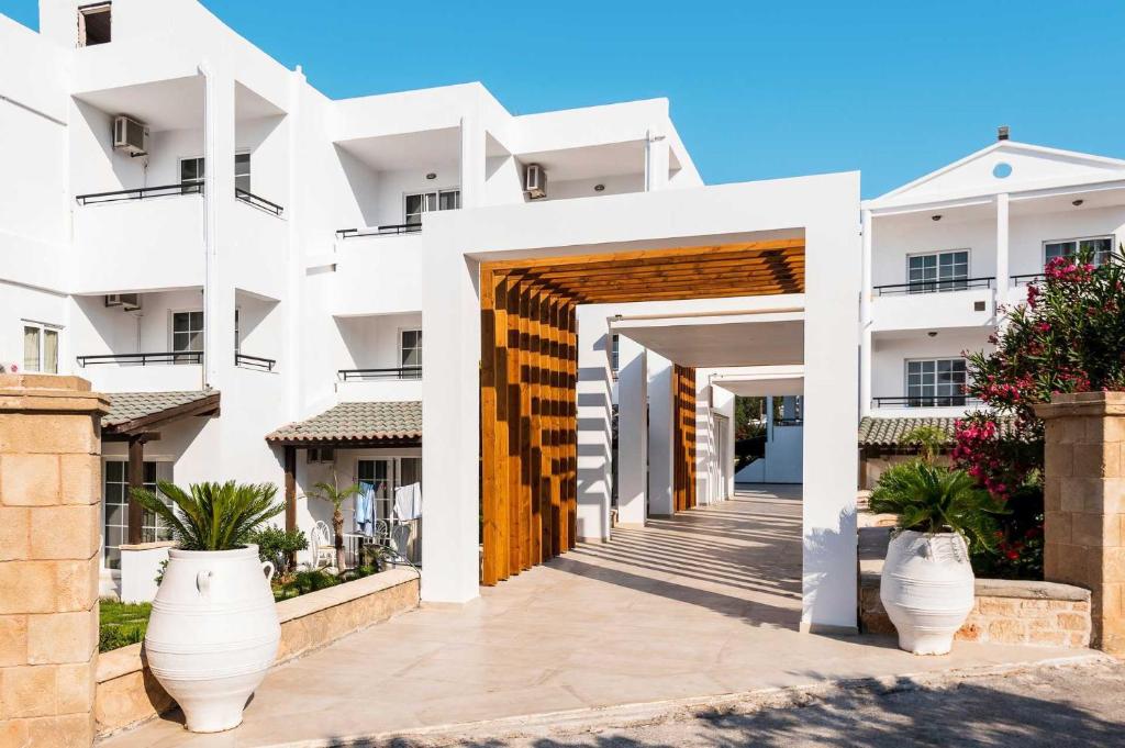 a facade of a white apartment building with a wooden doorway at Elvita beach hotel in Lartos