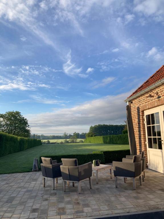a patio with chairs and a table and a field at Maison Lion Luxe gastenverblijf in Borgloon
