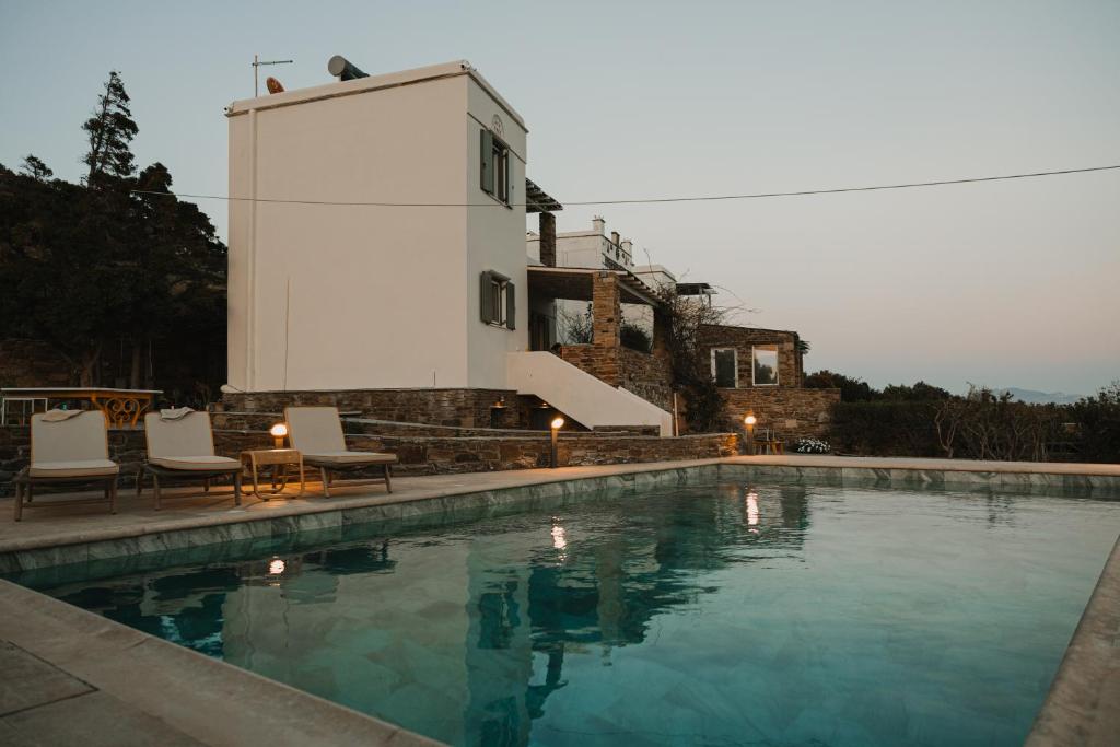 a swimming pool with two chairs and a building at Dinora Stone Villa, Pool & Sea Views in Tinos in Agios Ioannis