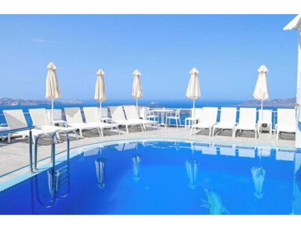a swimming pool with white chairs and a view of the ocean at Kafieris Blue in Firostefani