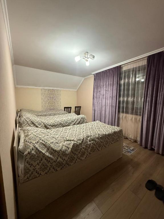 a bedroom with a bed and a window with purple curtains at Mama Nuris guest house in Karakol