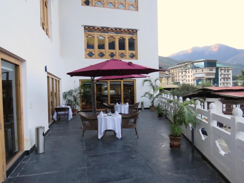 um restaurante com mesas e cadeiras brancas e guarda-sóis roxos em CityHotel, Thimphu em Thimphu