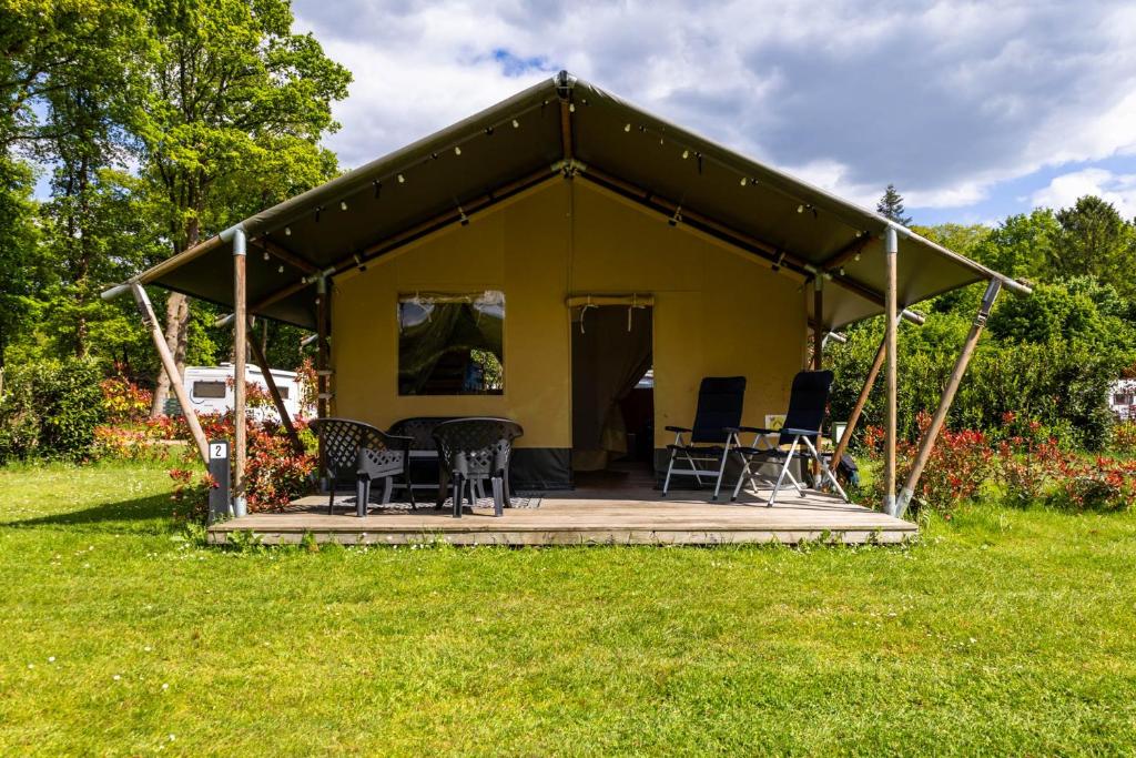 a yellow tent with chairs and tables in a field at Safaritent bij speeltuin voor gezinnen op groen rustig park op de Veluwe in Epe