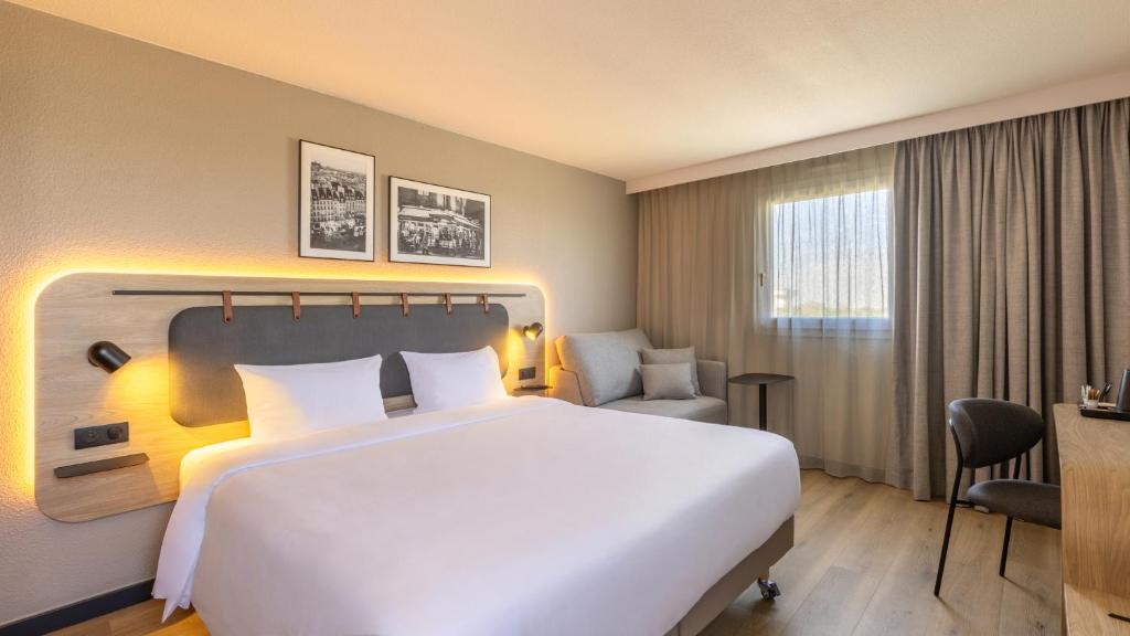 a hotel room with a large white bed and a chair at Campanile PRIME - Le Blanc Mesnil in Le Blanc-Mesnil