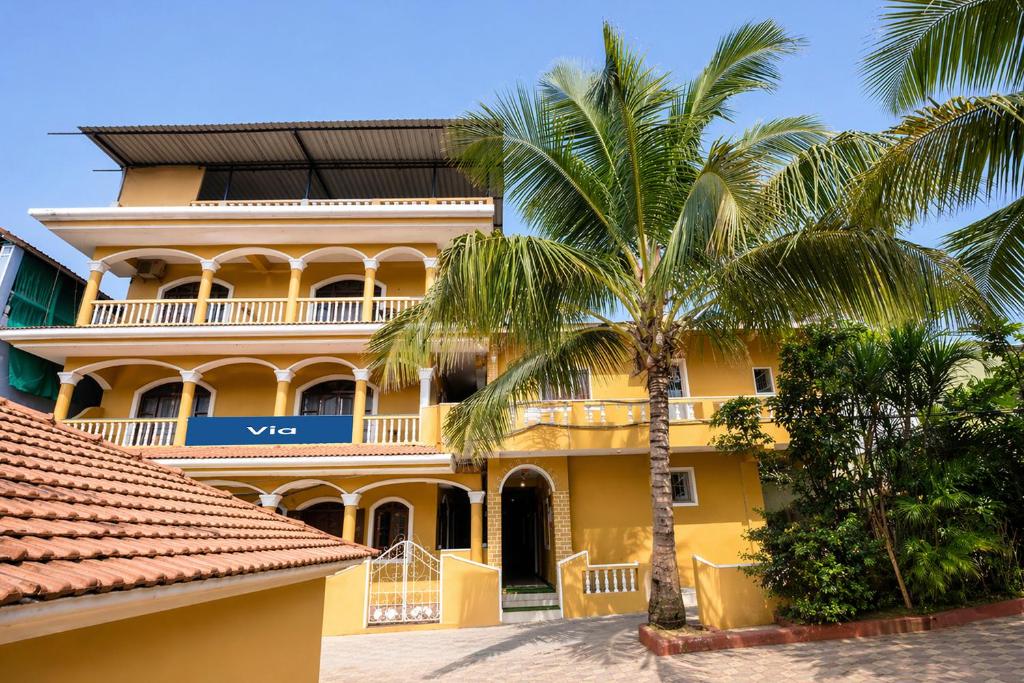 a yellow building with palm trees in front of it at Via Romeo's Stay - A Beach Property in Baga