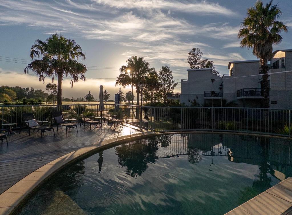 a swimming pool with palm trees and a building at Corrigans Cove Resort Batemans Bay in Batemans Bay