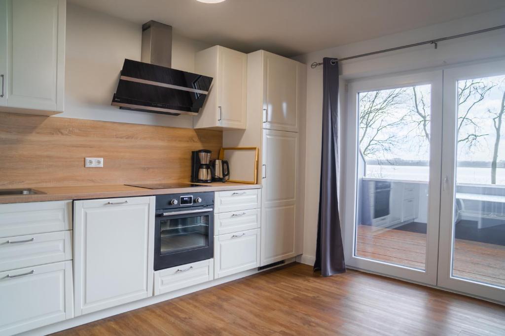 a kitchen with white cabinets and a sliding glass door at Schleiblick App 17 in Rabenkirchen-Faulück