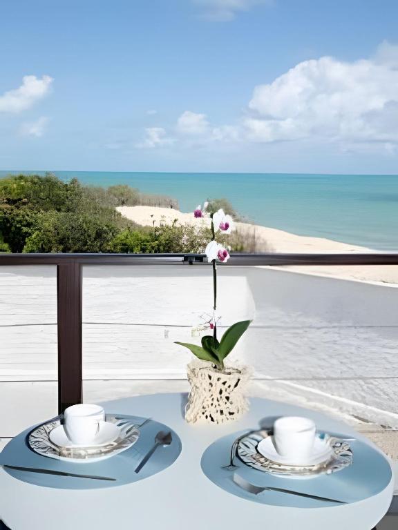 a table with two plates and cups on a balcony with the ocean at Sea View + Pool | Cliffs Mar 209 in Pipa
