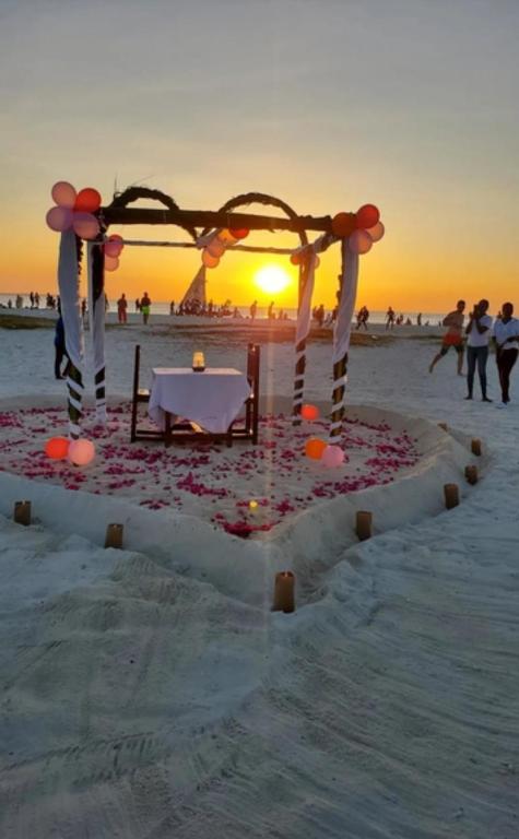 a table in the sand on the beach at sunset at Sun house kendwa beach in Kendwa