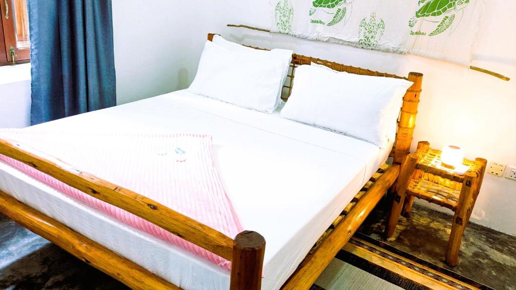 a wooden bed with white sheets and pillows at The Hub Train House Hakuna Matata in Zanzibar City