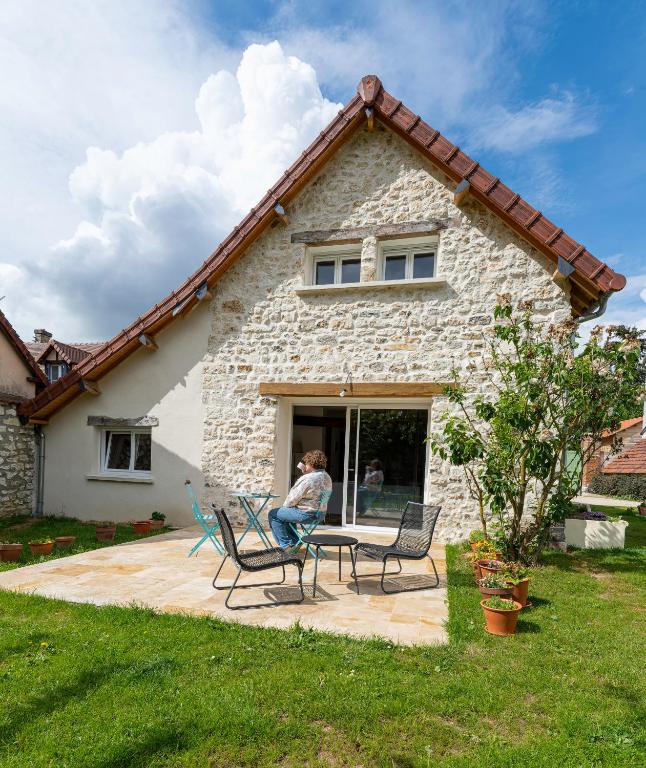 a woman sitting on a patio in front of a stone house at Ô Bois Jer'Home in Bois-Jérôme-Saint-Ouen