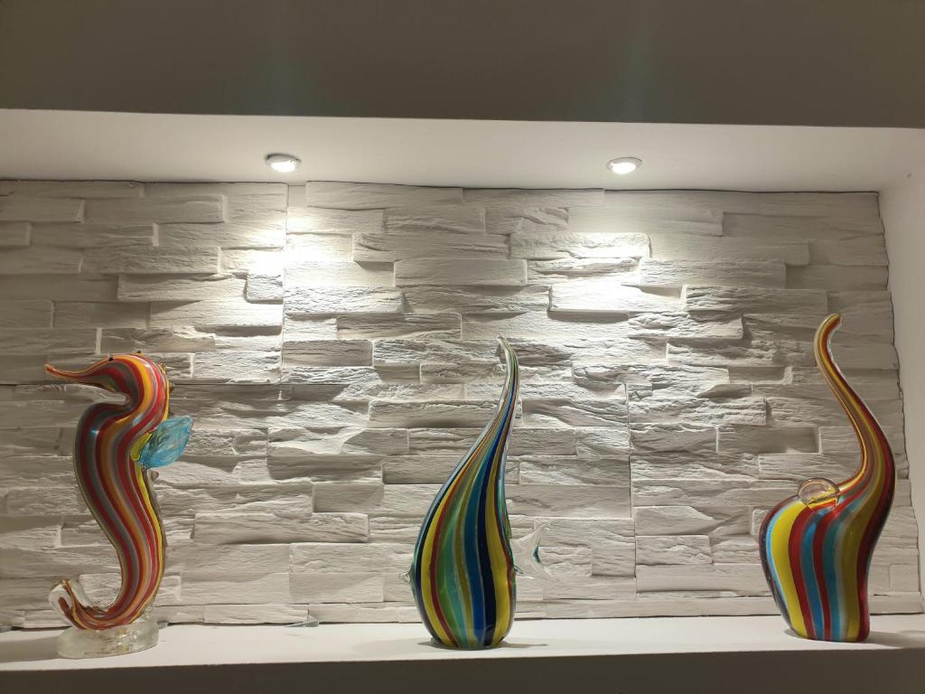 Sculture in vetro colorato illuminate su parete in pietra bianca, dettaglio degli spazi comuni