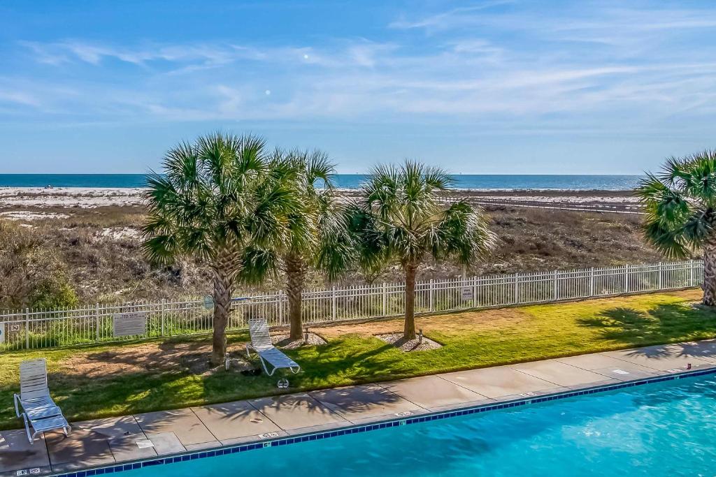 a pool with palm trees and the ocean in the background at Gulf-front condo with lock-out feature shared pools & amazing views in Dauphin Island