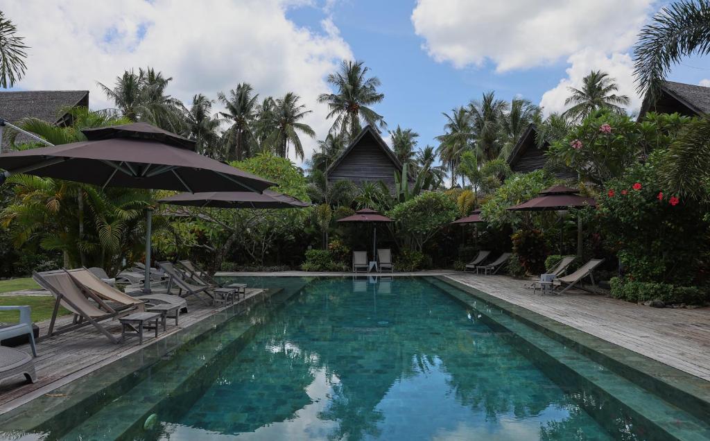 a pool with chairs and umbrellas next to a resort at Kaimana Resort Siargao in General Luna