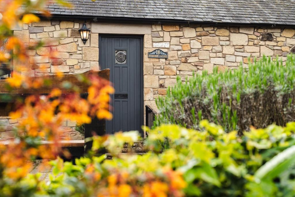 a stone house with a black door and some flowers at Blueberry Cottage in Wooler