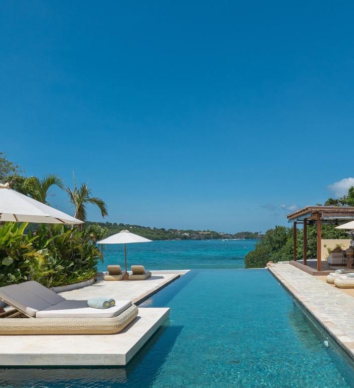 a pool with chairs and umbrellas next to the water at Private Oceanfront Villa Kingfisher - 20m Infinity Pool in Nusa Lembongan