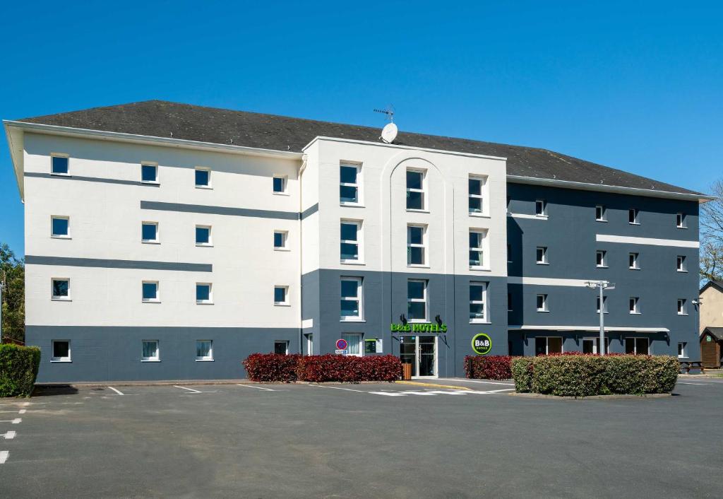 a large white building with a parking lot at B&B HOTEL Bayeux in Bayeux
