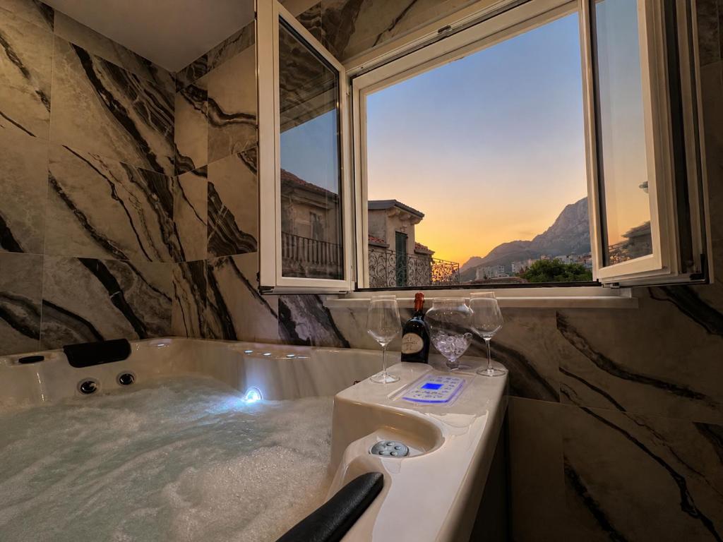 a bath tub with two wine glasses and a window at Centrium Makarska in Makarska