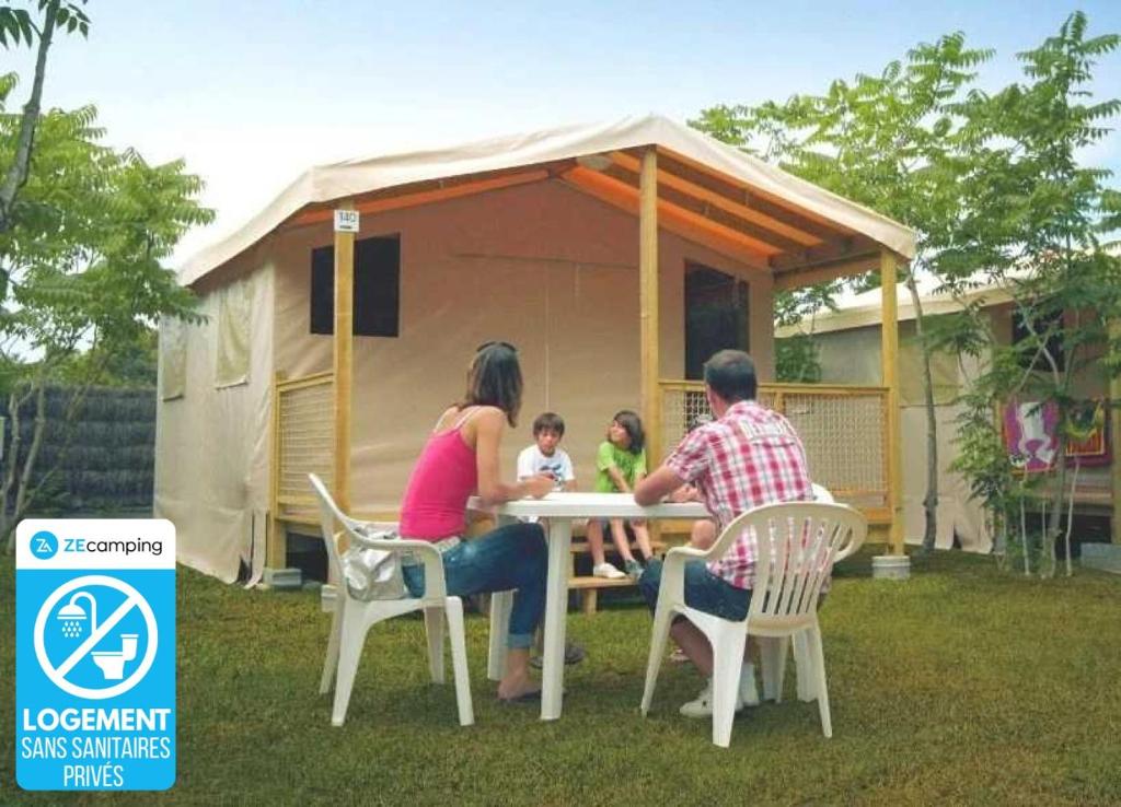 a family sitting at a table in front of a house at ZEcamping familial avec parc aquatique - chiens acceptés in Saint-Jean-dʼOrbetiers