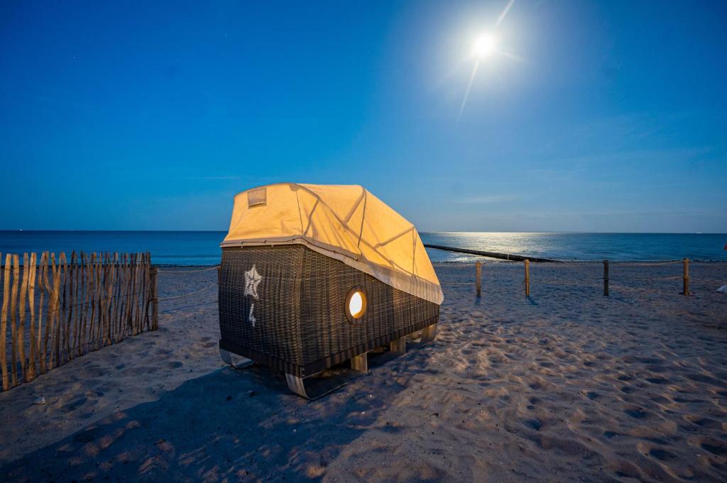 a cage on a beach with the sun in the sky at Schlafstrandkorb Nr 5 in Kellenhusen