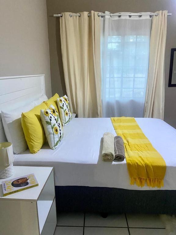 a large white bed with yellow sheets and a window at Maun East Gate Guesthouse in Maun