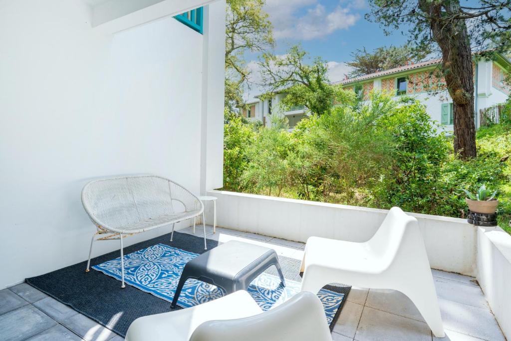 a patio with white chairs and a chair and a window at Appartement proche du port in Capbreton