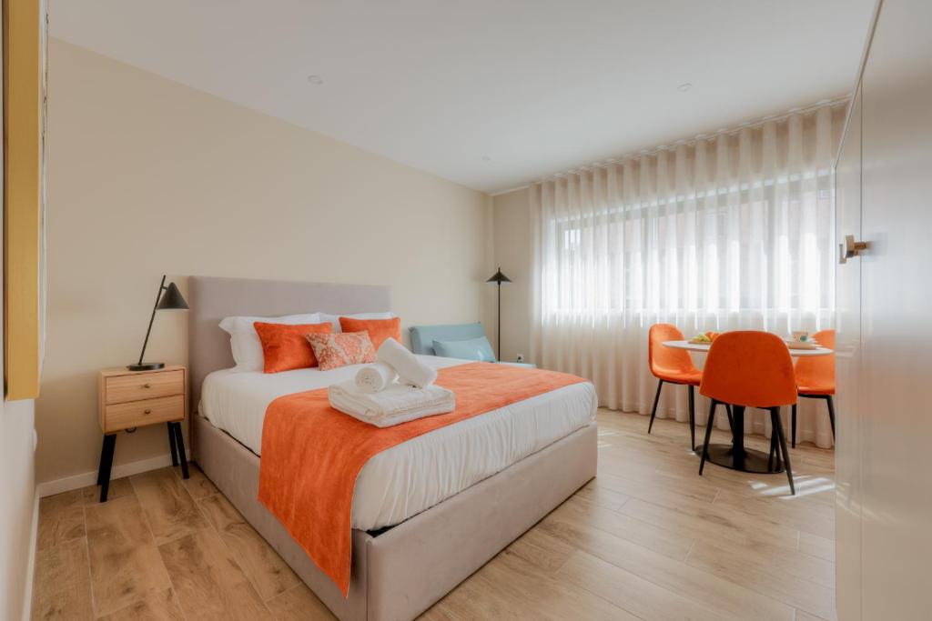 a bedroom with a bed with an orange blanket and a table at Calvário Suites l in Chaves