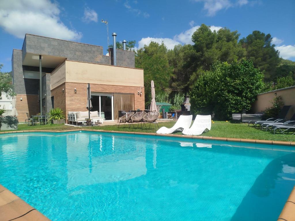 a swimming pool with white chairs and a building at Can Vinyals Holiday Home in Castellar