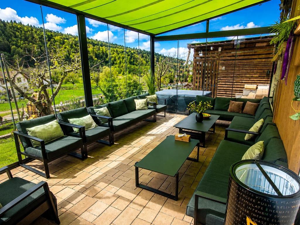 a patio with green couches and tables and windows at Cazare Colibita - Casa Lipan cu jacuzzi, foișor și loc de joacă in Colibiţa