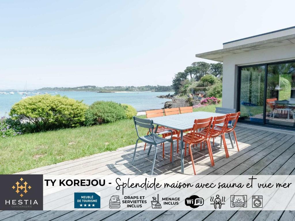 a table and chairs on a deck with a view of the water at TY KOREJOU - splendide maison avec sauna les pieds dans l'eau in Plouguerneau