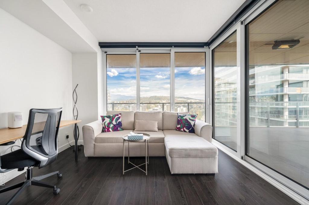 a living room with a couch and a desk and window at Bright & Cozy 1BR Steps to Brentwood mall in Burnaby