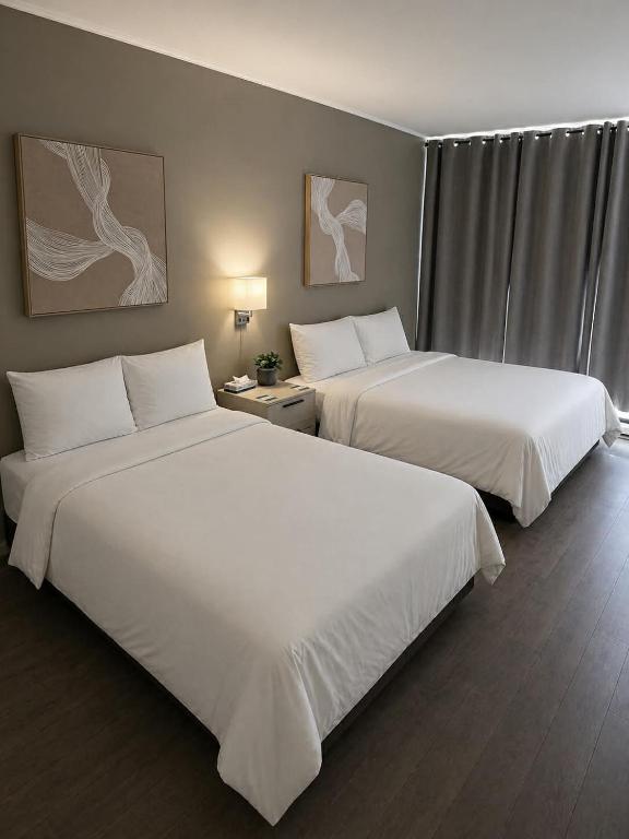 two beds in a hotel room with white sheets at Hôtel Normandie in Rimouski