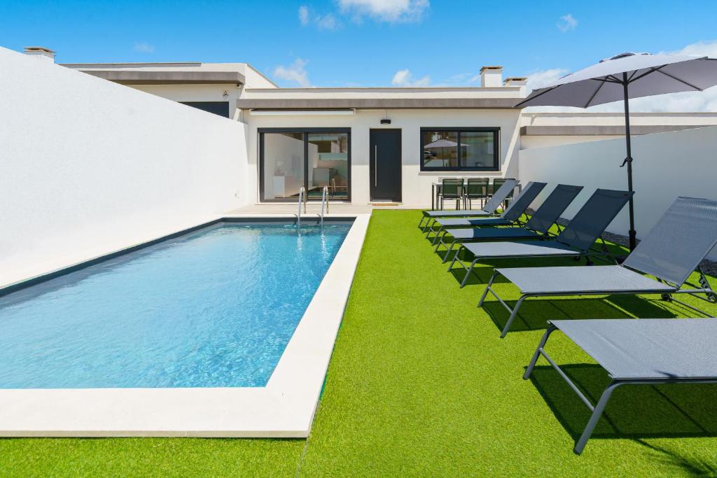 a swimming pool with lawn chairs and an umbrella at Villa Emilio with private pool in Mariquiteira