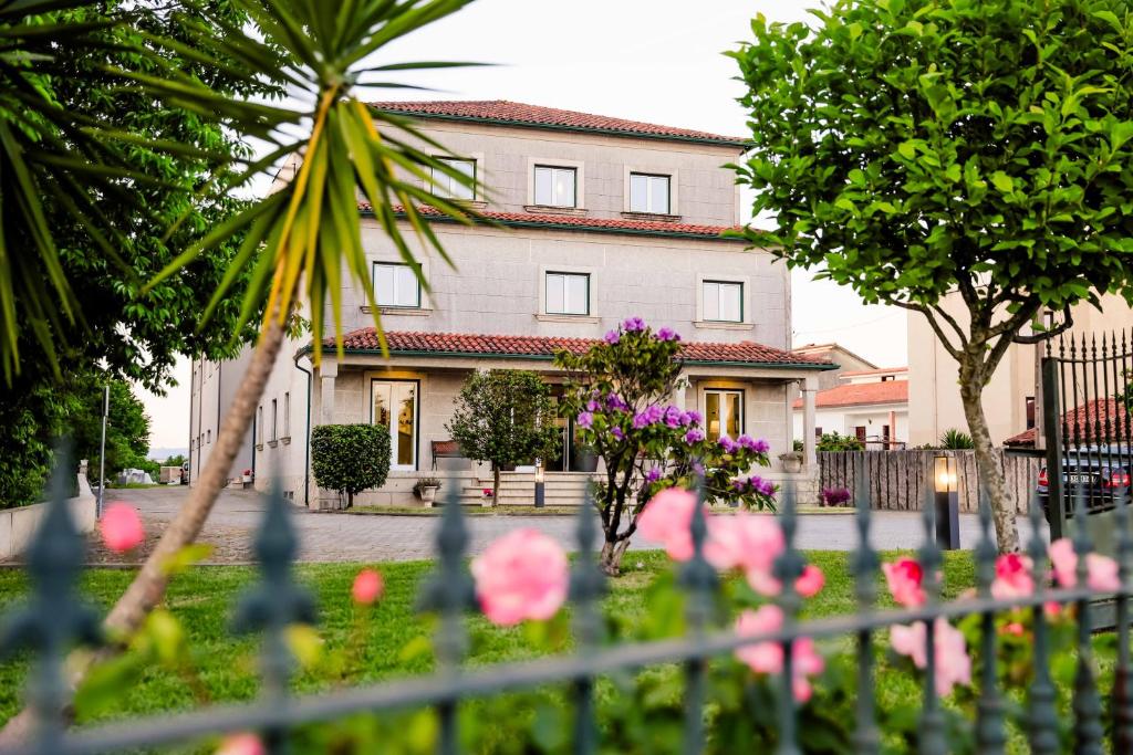Ein Haus mit rosa Blumen vor einem Zaun in der Unterkunft Hotel Flor do Minho in Valença