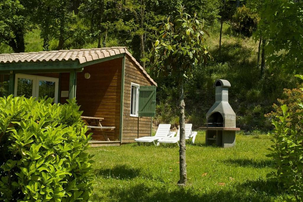 a small cabin with a grill and chairs in the grass at Camping Verte Rive in Saint-Laurent-de-Cerdans