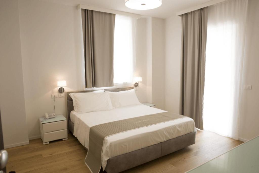 a white bedroom with a bed and a window at Boutique Hotel Enia in Prato