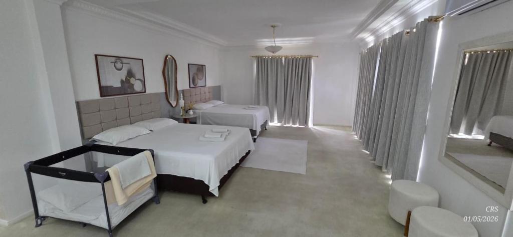 a white bedroom with two beds and a mirror at Grand Ville Hotel in São Lourenço
