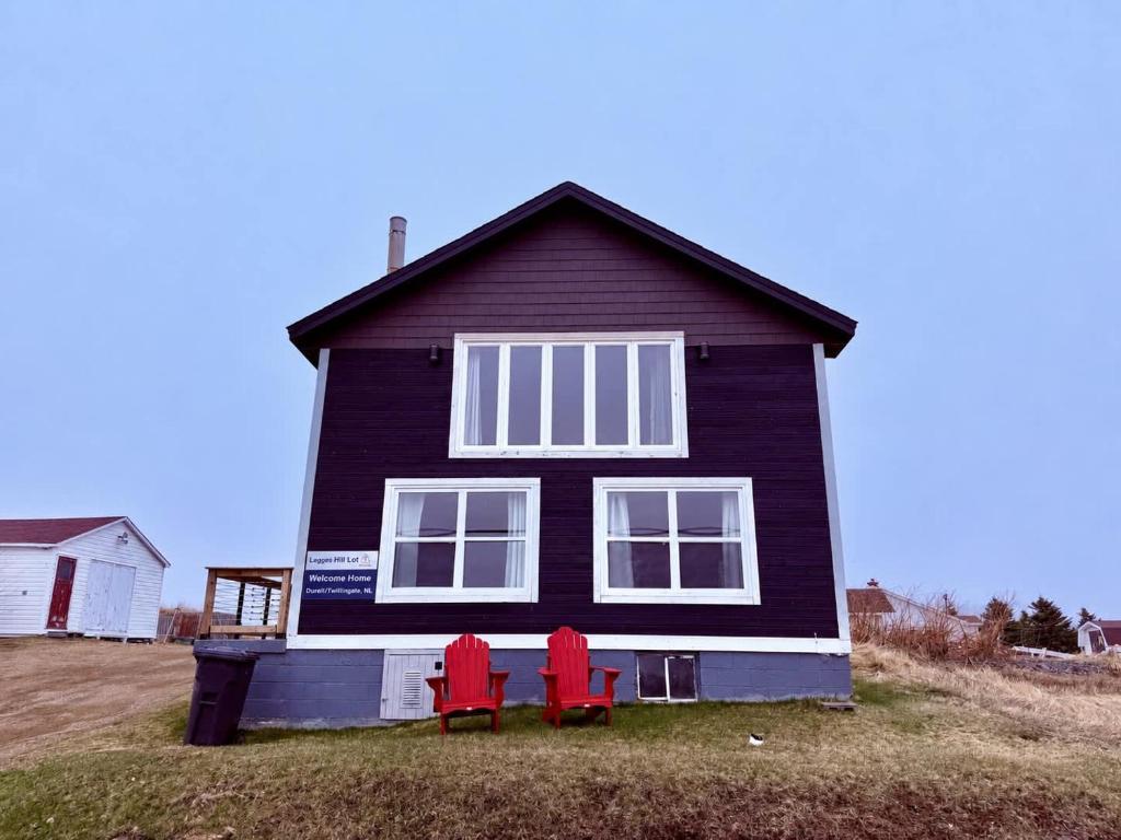 two red chairs in front of a black house at Legges Hill Loft in Twillingate