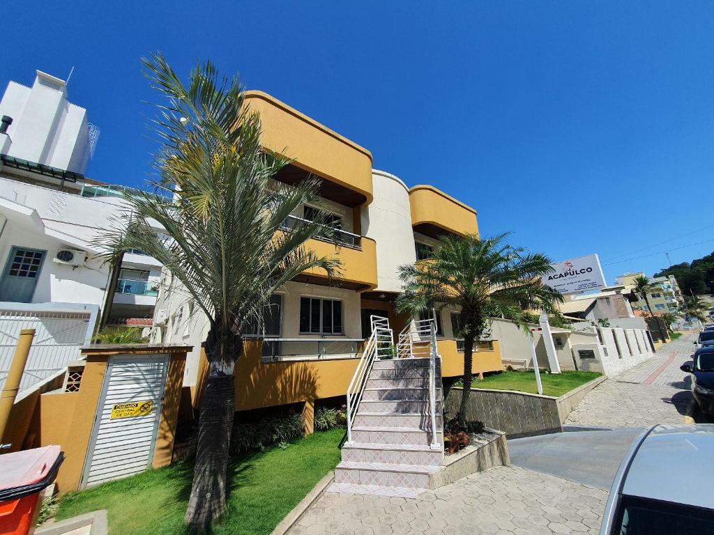 a yellow building with palm trees in front of it at Pousada Acapulco in Bombinhas