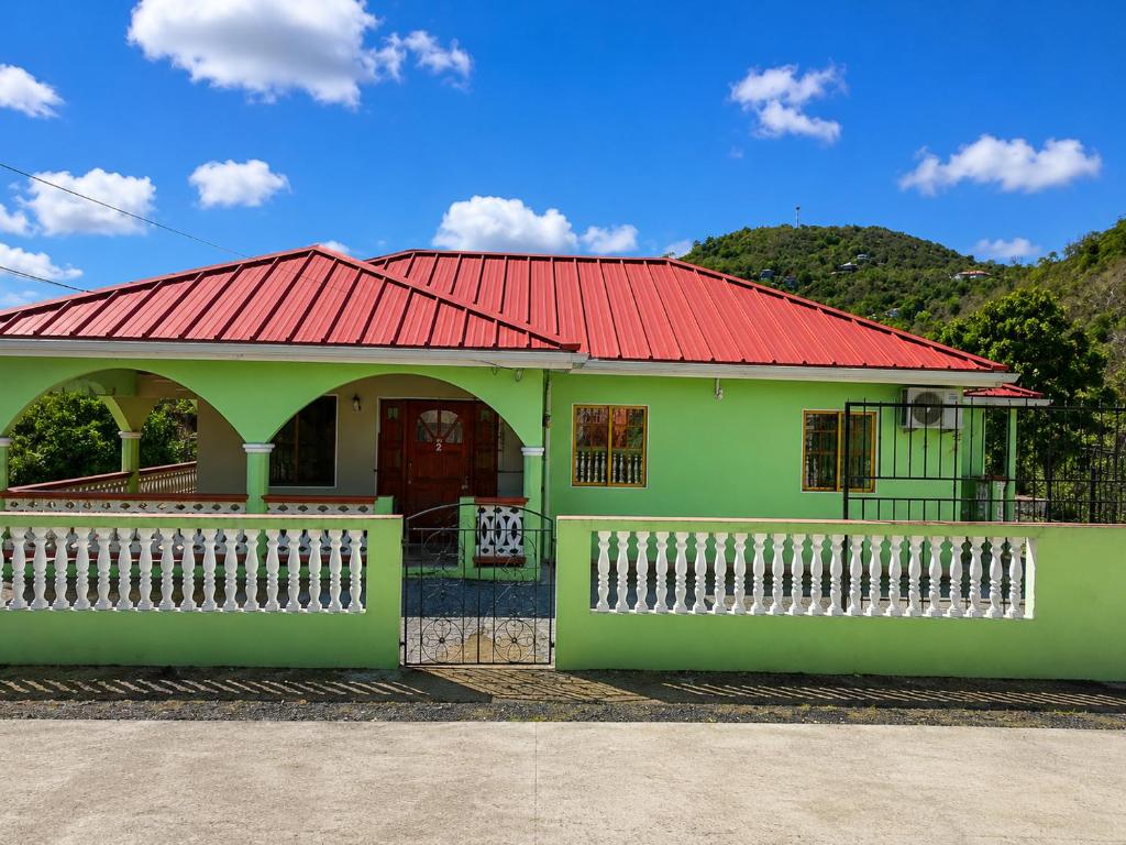 a green house with a red roof and a white fence at Paradise Inn in Laborie