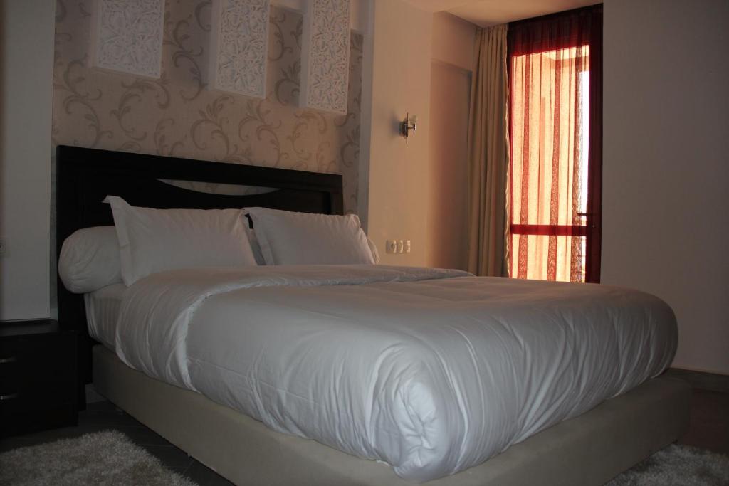 a bedroom with a large bed with white sheets and a window at Résidence La Place in Laayoune