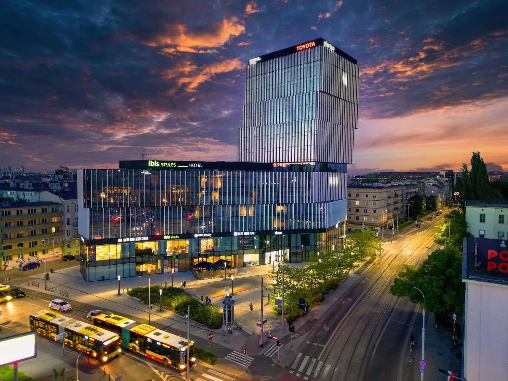 a tall glass building with buses in a city at Ibis Styles Wroclaw Centrum in Wrocław