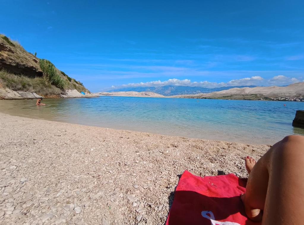 a person sitting on a beach near the water at Apartments Vuleta in Pag