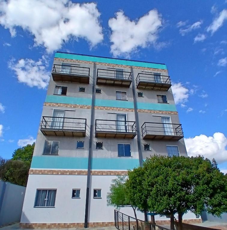 a tall white building with balconies and a tree at Conforto e Praticidade, Studio para 2 pessoas in Ponta Grossa