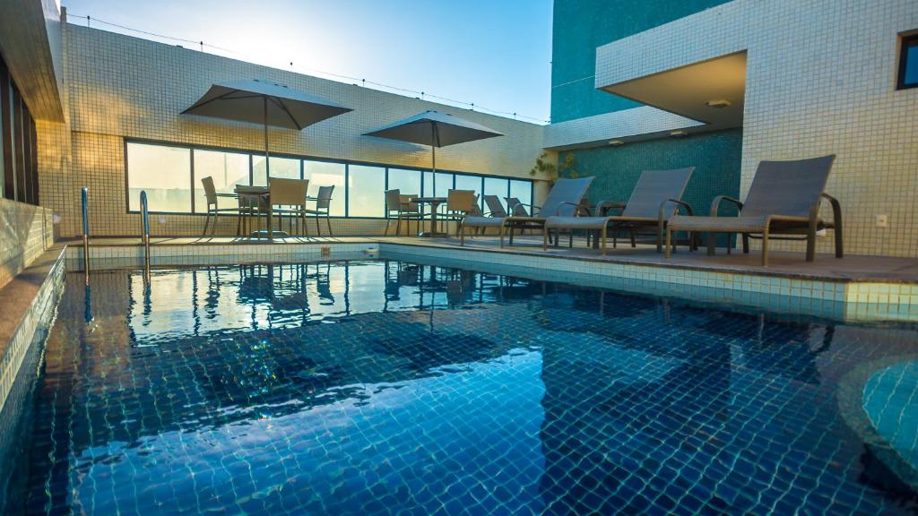 uma piscina com cadeiras e mesas num edifício em Mais Hotel Aeroporto Salvador em Lauro de Freitas