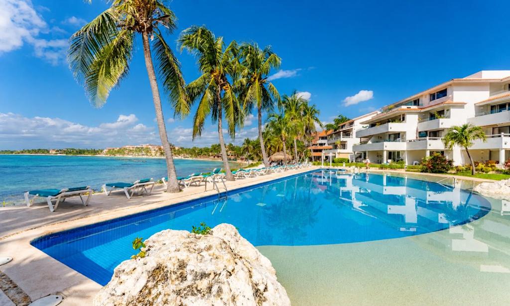 a resort swimming pool with palm trees and the ocean at Beachfront condo with loft and sea views in Puerto Aventuras