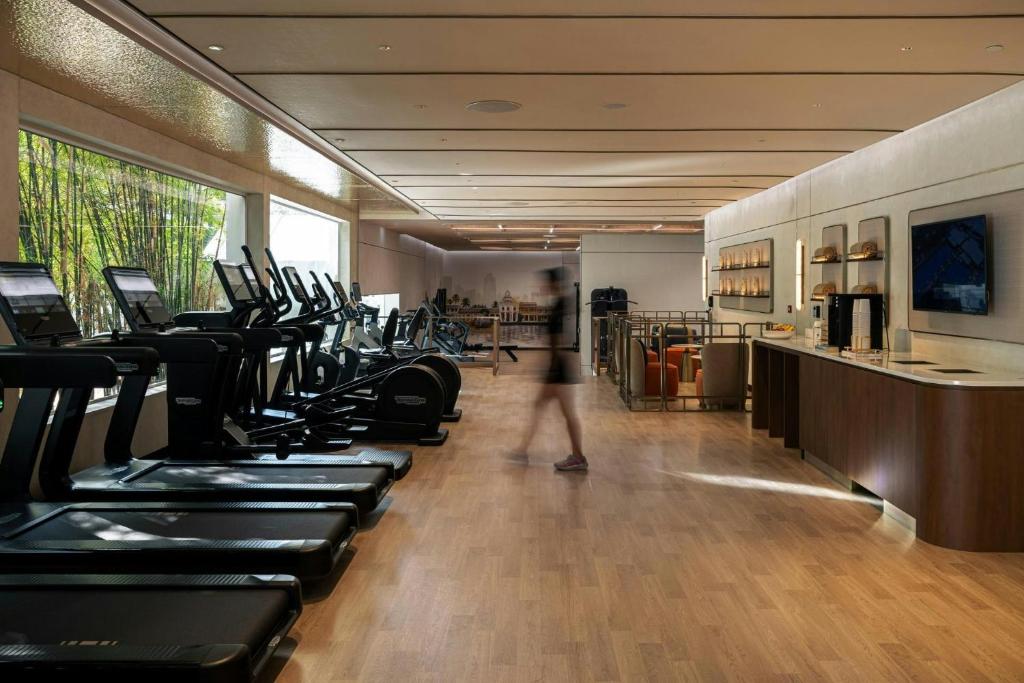 A bright hotel gym with a long row of cardio machines and a wood-floored training area.