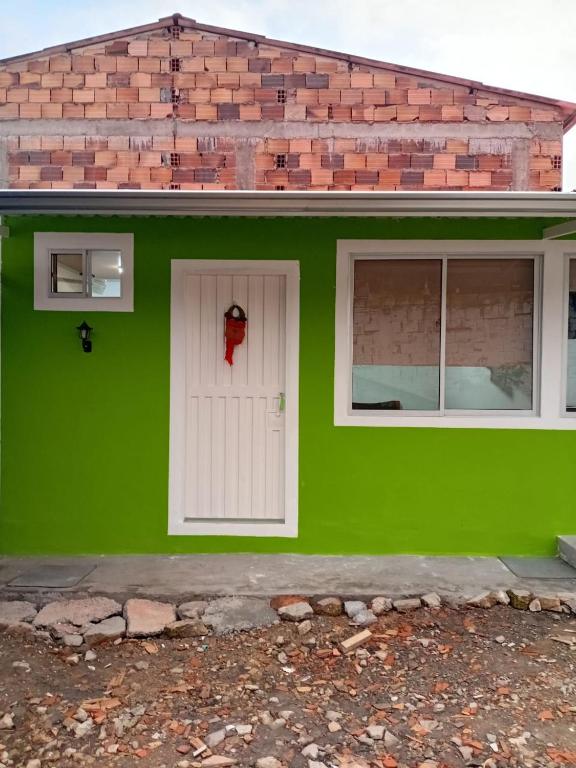 a green house with a white door and two windows at casa demaiz in Choachí