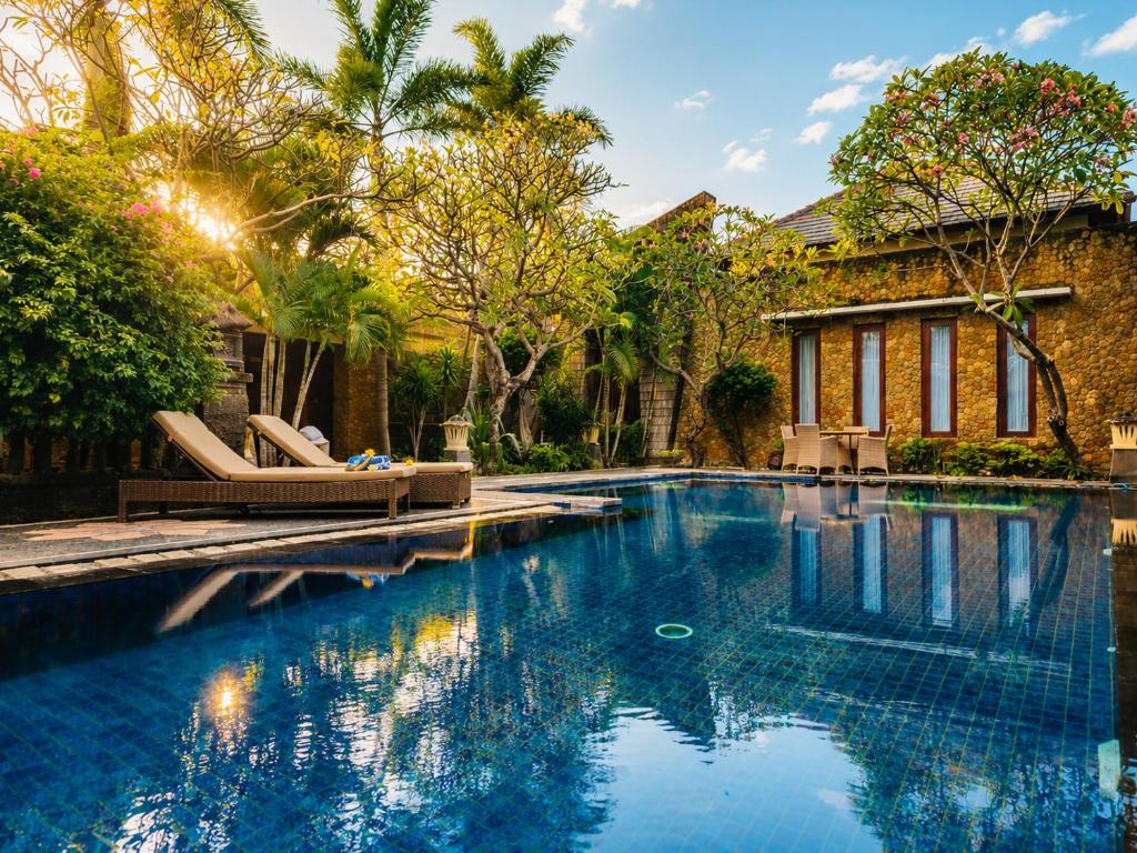 a swimming pool with two lounge chairs in front of a house at Vamana Resort - CHSE Certified in Gili Trawangan