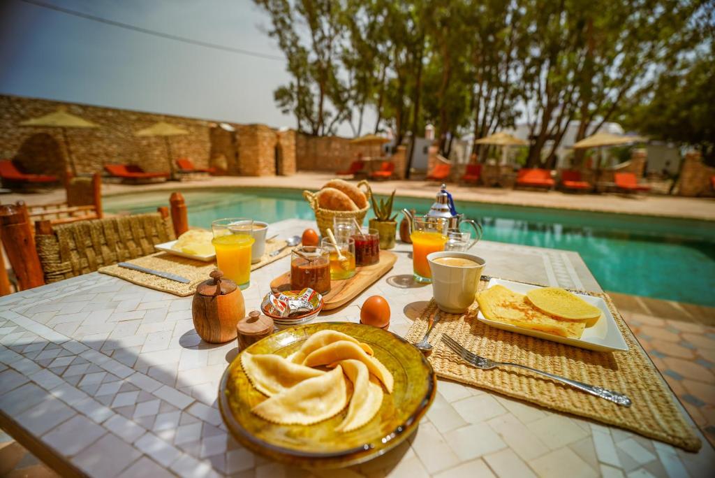 a table with breakfast foods and drinks and a pool at Maison d'hôtes Villa Latifa Essaouira in Essaouira